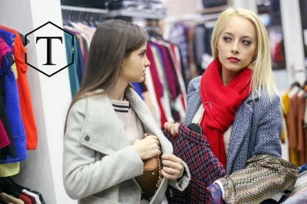 Two women in a store, one of them hiding a piece of clothing.